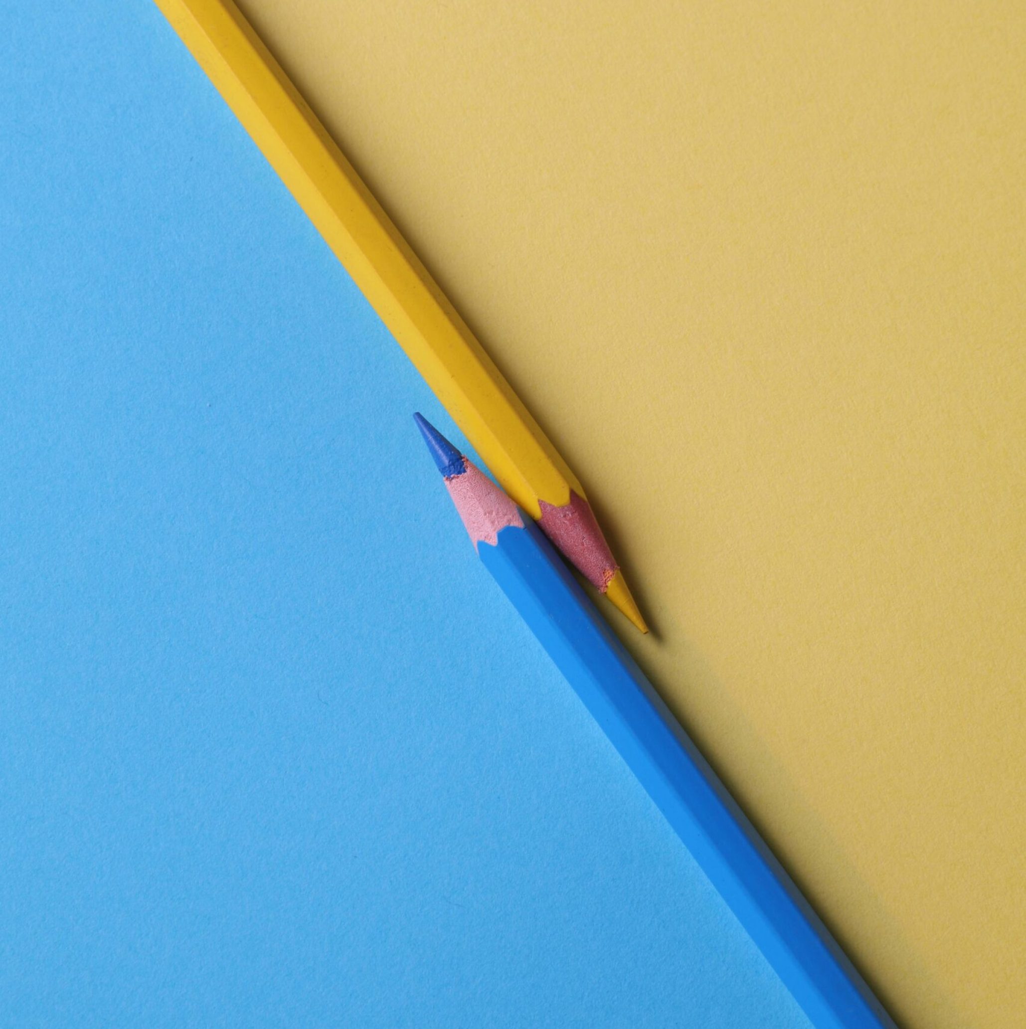Close-up of vibrant yellow and blue colored pencils on contrasting paper backgrounds.