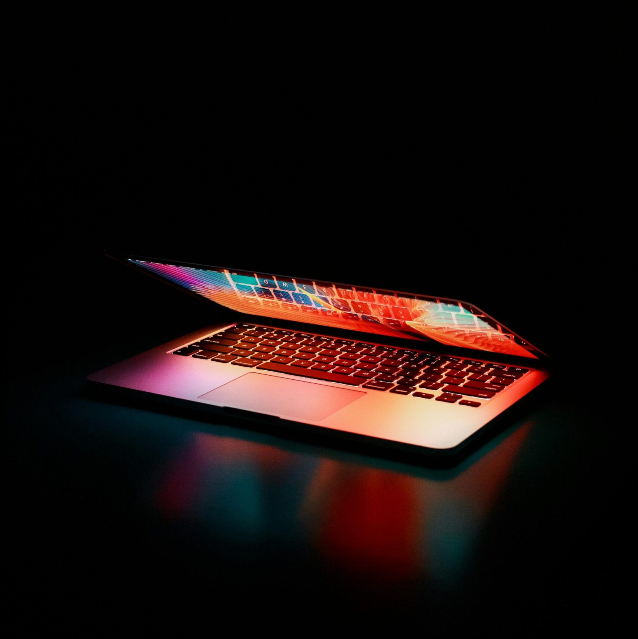 Laptop partially opened, emitting vibrant multicolored lights in dark setting.